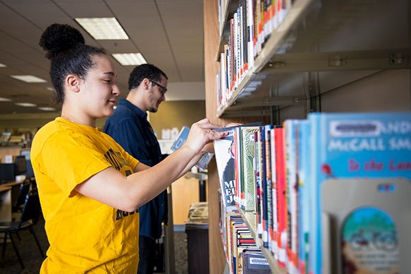 Two people looking at book selves and pulling out a book