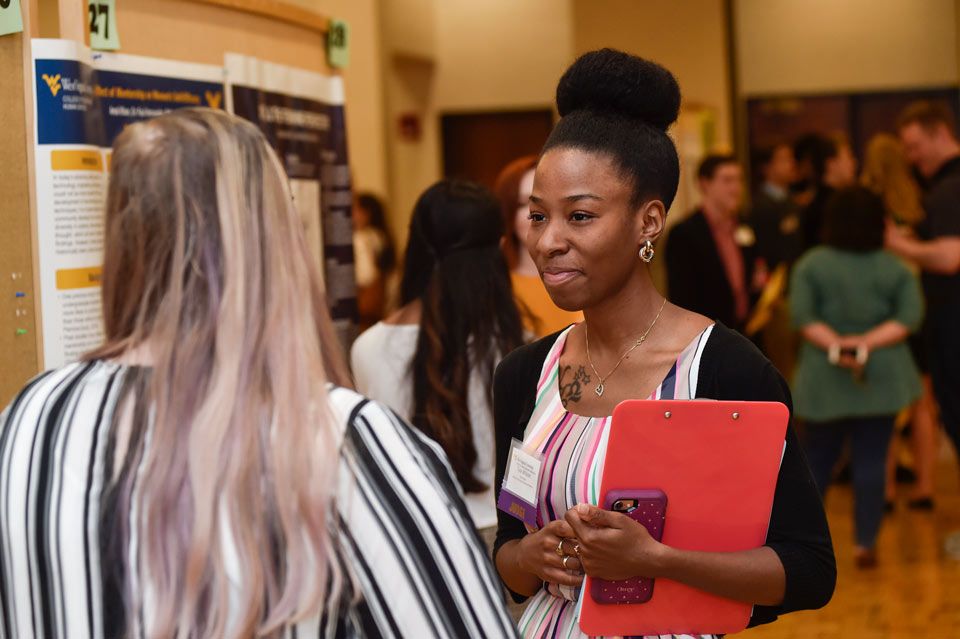 Smiling woman listening to a presenter presenting a research poster.