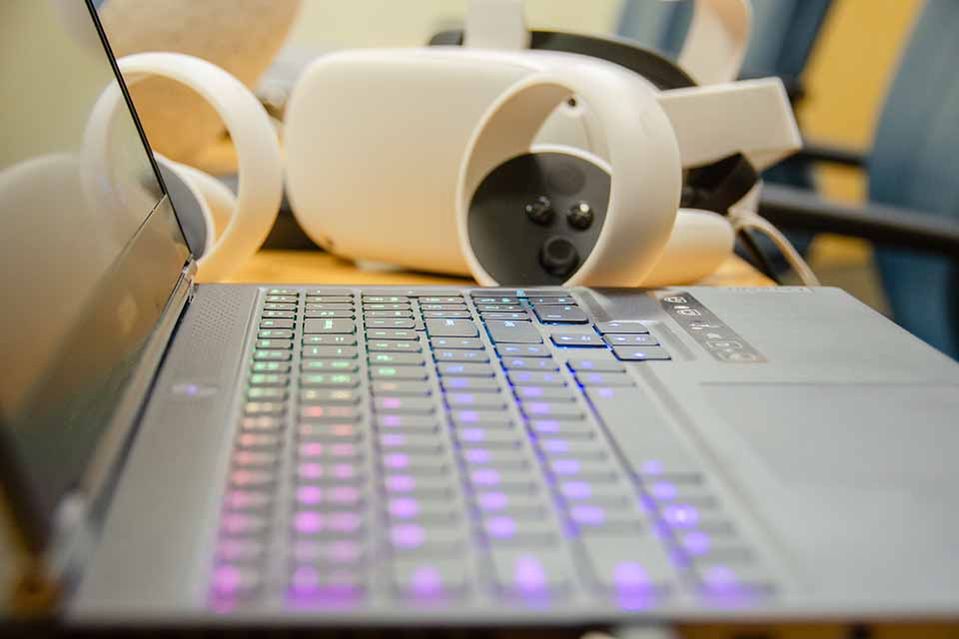 a keyboard of a laptop with a virtual reality headset in the background