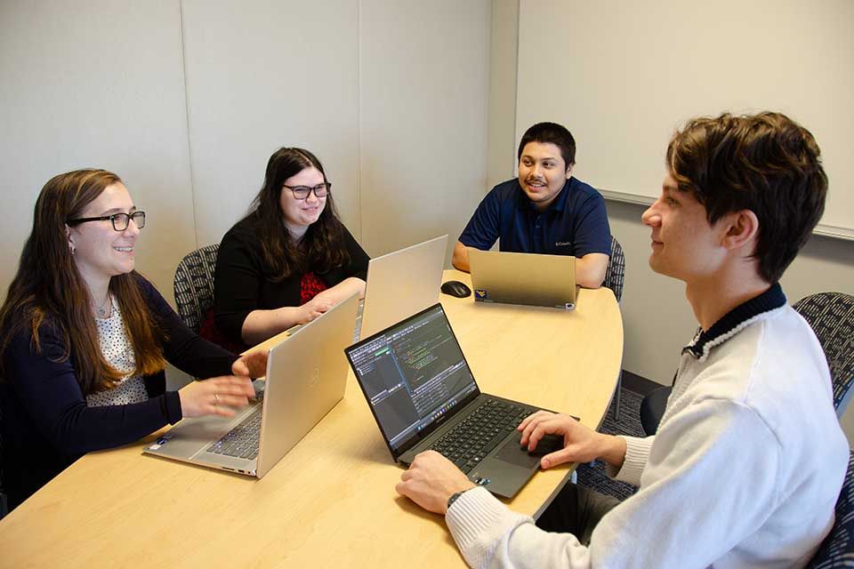 Four persons around a table with laptops open